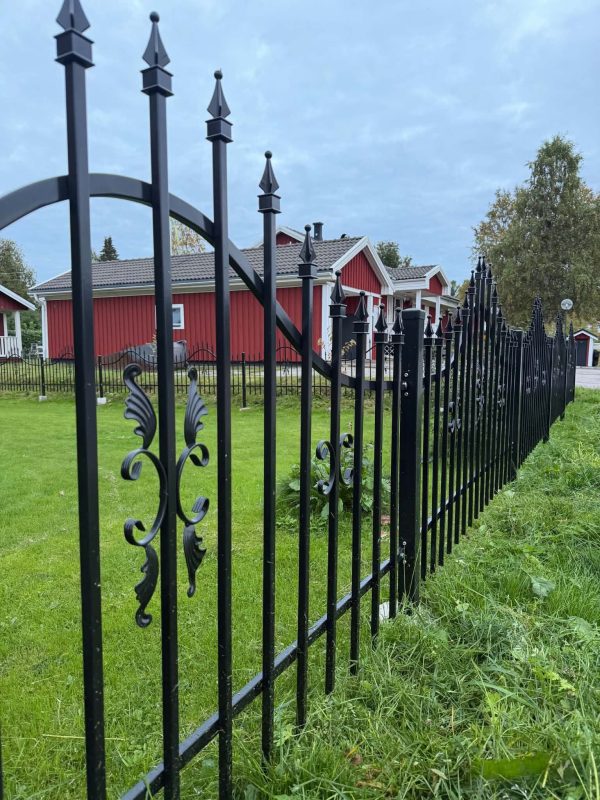 Svart smidesstaket längs en grön trädgård