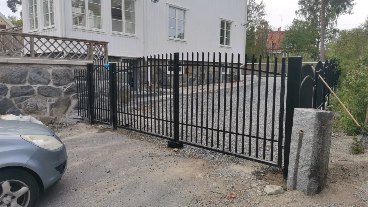 Svart dubbelgrind och staket vid en grusad infart